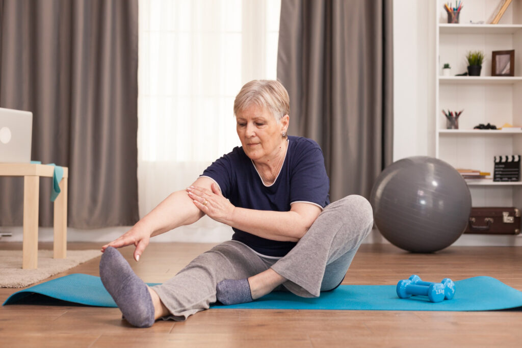 Vrouw rekt zich uit op een yoga matje en moet uitkijken voor achillespees klachten na het sporten.