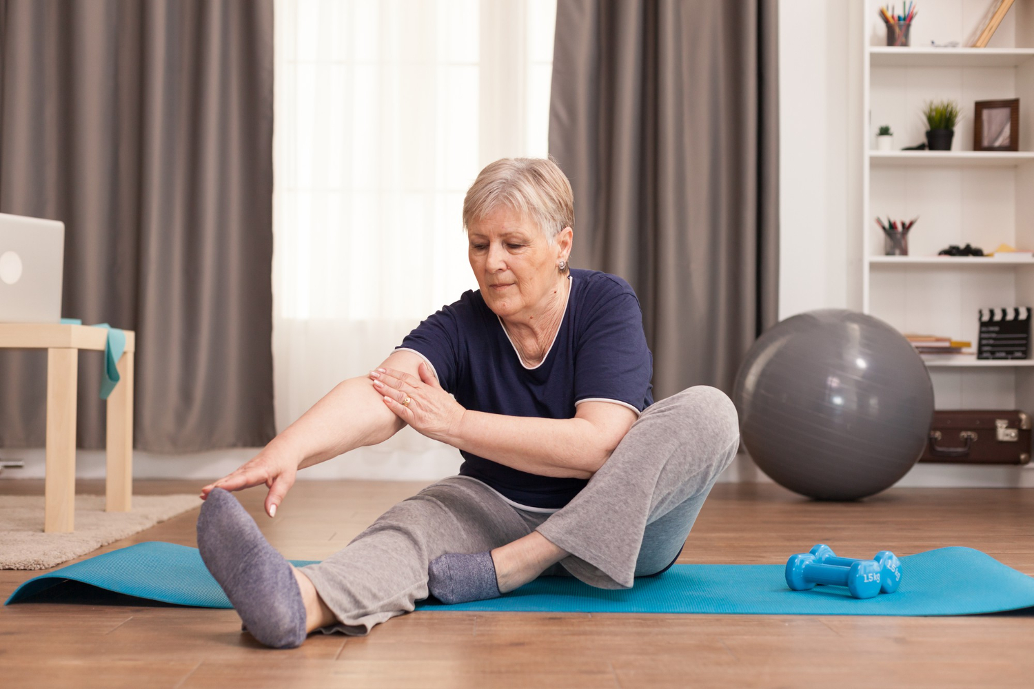 Vrouw rekt zich uit op een yoga matje en moet uitkijken voor achillespees klachten na het sporten.